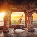 Woman doing yoga in ruined ancient temple with columns at sunset in Hampi, Karnataka, India